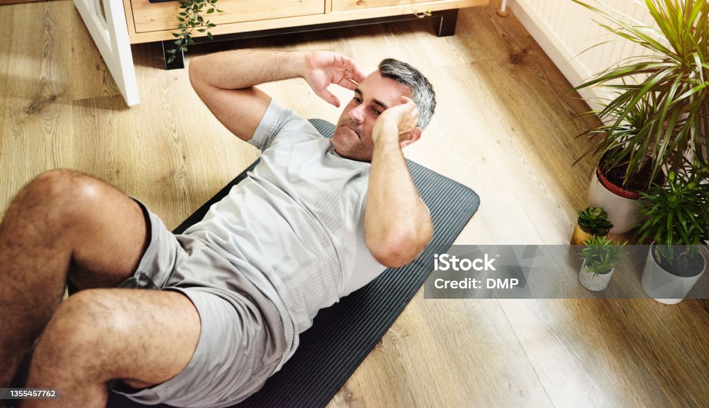 Shot of a mature man doing crunches to strengthen his core at home I can feel my abs coming in Sit-ups Stock Photo