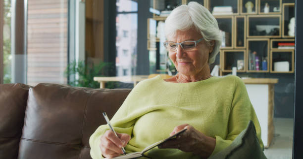 foto de una mujer mayor escribiendo en un diario en casa - diary fotografías e imágenes de stock