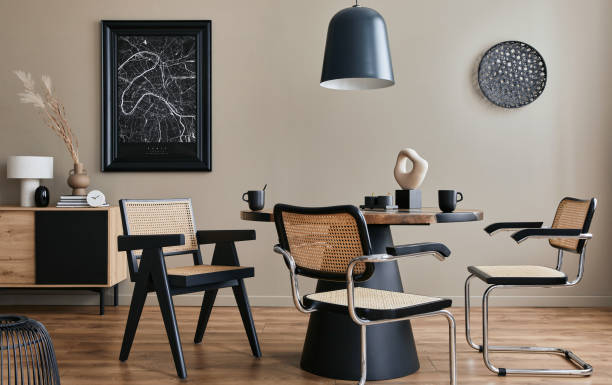 Modern composition of dining room interior with design wooden table, stylish chairs, decoration, teapot, cups, vessel, commode, black mock up poster map and elegant accessories in home decor. Template stock photo