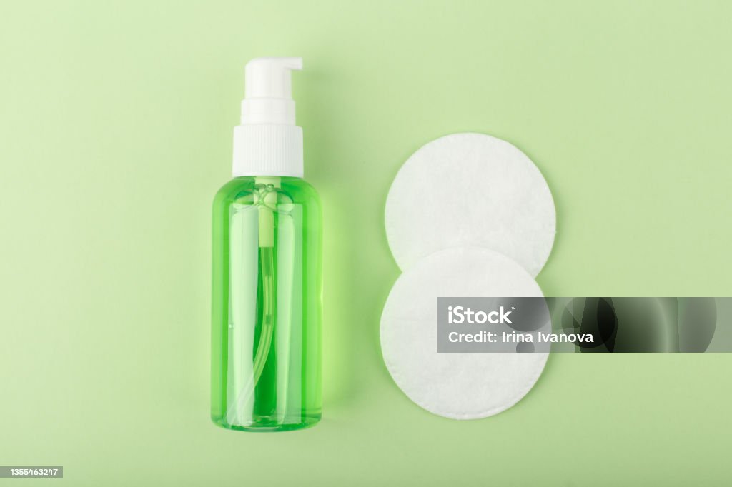 Top view of green cleansing foam or gel for make up removing and cotton pads on bright green background. Top view of green organic cleansing foam or gel for make up removing in transparent tube and cotton pads on bright green background. Concept of daily skin care or anti acne treatment Removing Stock Photo