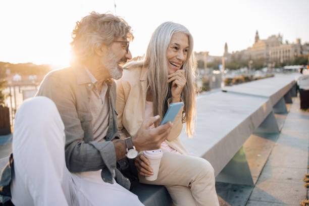 Mature couple on vacation enjoying outdoors and having fun online Portrait of a mature couple enjoying their journey in Barcelona, taking a break on the street and using a smartphone. 60 69 years stock pictures, royalty-free photos & images