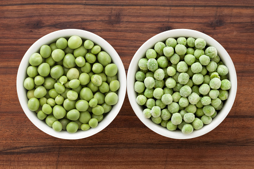 Top view of two bowls side by side with raw and frozen green peas