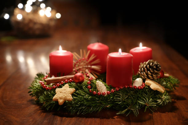 istock Third Advent - decorated Advent wreath from fir branches with red burning candles on a wooden table in the time before Christmas, festive bokeh in the warm dark background, copy space, selected focus 1355470887