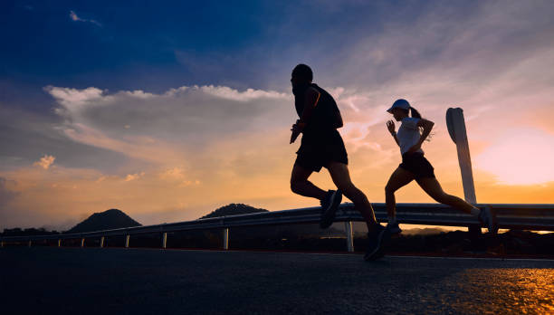 Two runners are running on the road during sunset. Two runners jogging in the evening on a road during the sunset. Athletes always train and prepare their bodies to be healthy. showing movement. Running stock pictures, royalty-free photos & images