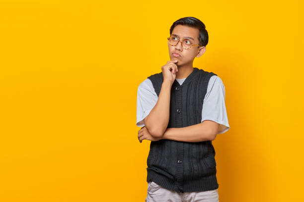 istock Pensive handsome young man rubbing chin and thinking question on yellow background 1355477300