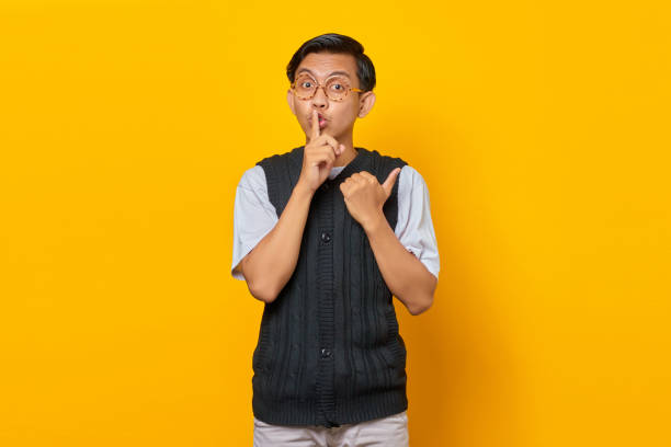 istock Handsome asian man making finger on lips, silent gesture and finger pointing at empty space over yellow background 1355477856