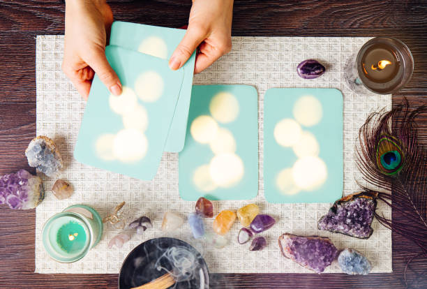 Deck with homemade divination Angel cards on white background, surrounded with semi precious stones crystals, candles burning. Selective focus on amethyst crystal angel figurine.