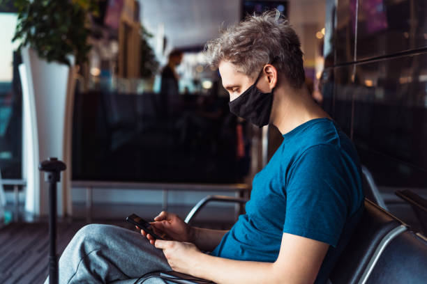 istock Man wearing face mask and using his phone while waiting for flight at airport terminal. New normal, digital nomad and freelance lifestyle. Traveling during pandemic and personal protection. 1355481137