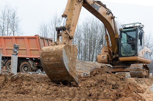 Photograph of an excavator loads a truck with construction sand.