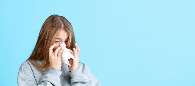 Flu. Portrait of young beautiful girl in warm winter clothes sneezes, snots isolated on navy color background in neon. Concept of emotions, facial expression, youth, aspiration. Copy space for ad