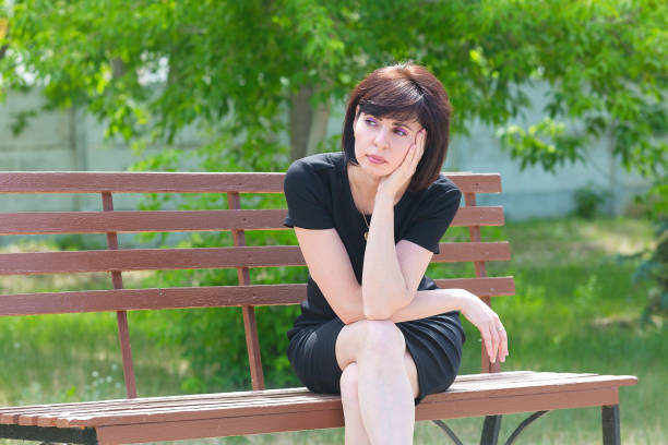 a sad brunette 35-40 years old sits on a bench with her chin propped on her hand and looks away"n - 35 40 years fotos imagens e fotografias de stock