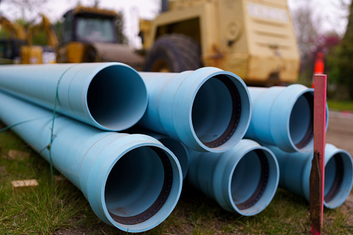 A view of blue pipe used to replace water main pipe system.  The setting has no people and there is large equipment in the background.