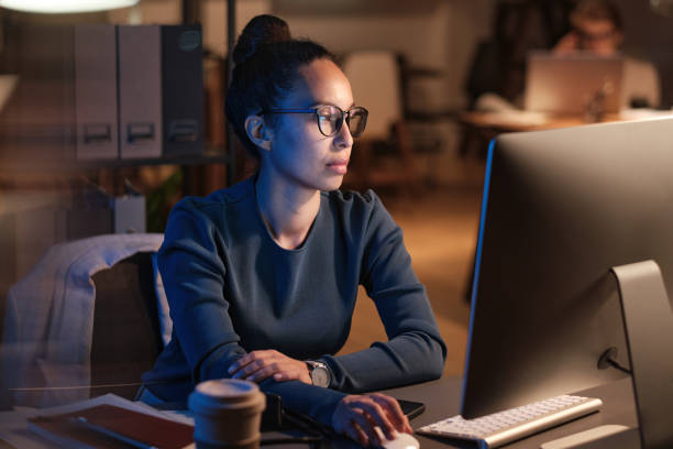 istock Serious young business lady in glasses sitting at table and using computer while preparing presentation at night 1355489638