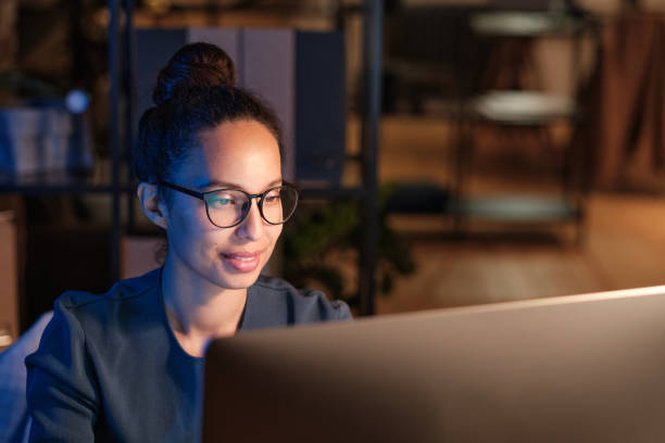 istock Positive young multiethnic woman in glasses using modern computer while working late in office 1355490467