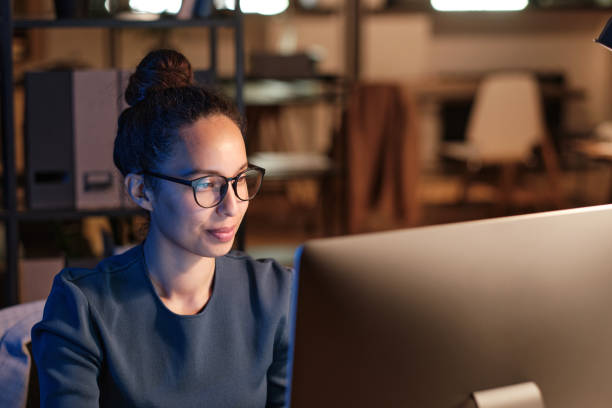 istock Content young biracial female office employee in glasses using computer while working at night 1355490515