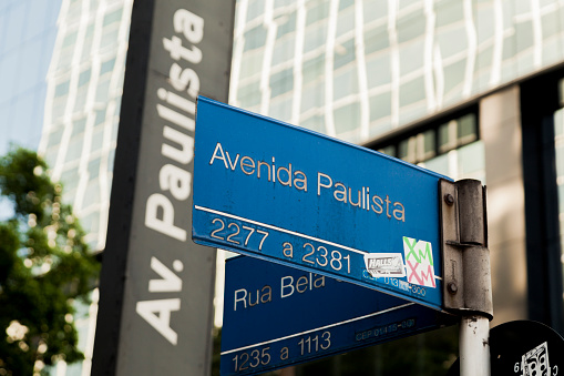Plate on the Paulista Avenue sign with mirrored buildings in the background during the day. Sign with Large urban center. usage marks. São Paulo avenue concept.