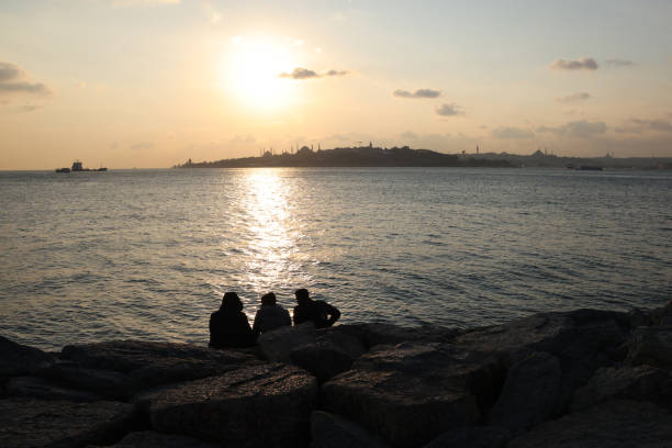 Istanbul, Turkey - November 15,2021: Three people sitting by the stone watching the Bosphorus at sunset