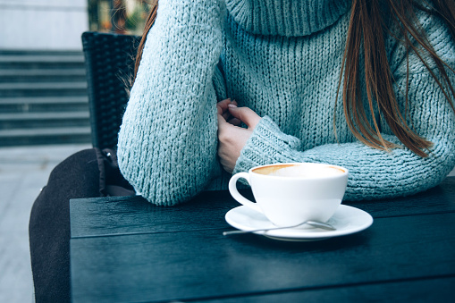 Woman in a cozy blue sweater drinking coffee in a street cafe. Cup of morning coffee. Noface