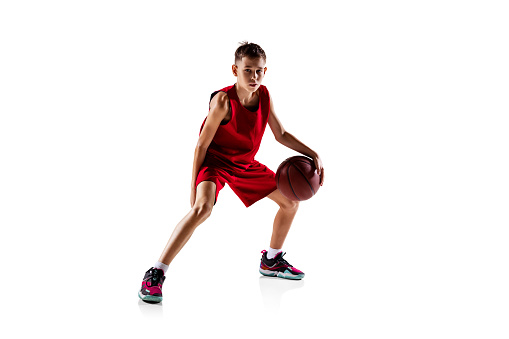 Winning game. Portrait of boy, basketball player in red uniform training isolated over white background. Dribbling. Concept of motivation, sport, action, movement, health. Copy space for ad