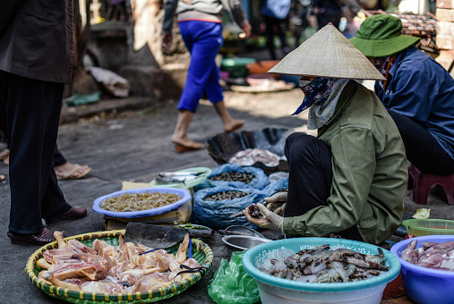Vietnamese people sit and sell chicken and other fresh food at a fresh market in the central market of Hanoi, Vietnam.