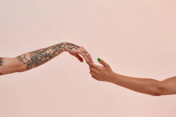 Closeup of two female arms reaching each other hand isolated over light pink background stock photo