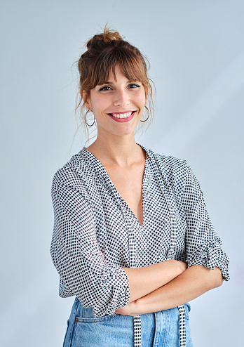 Vertical image of an adult woman smiling with her arms crossed looking at camera indoor