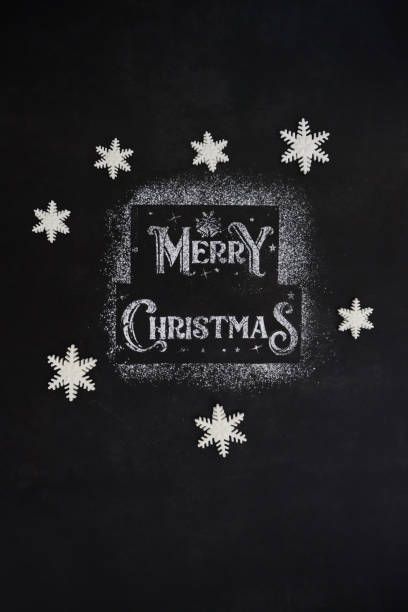 istock Image of Merry Christmas message stencilled with white icing sugar on black background surrounded by fondant icing snowflake shapes, elevated view 1355500666