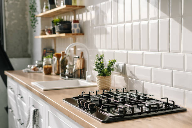 Kitchen in white tones with stove, sink and shelves Side view of scandinavian style kitchen interior in white tones with stove, sink and shelves. Luxury apartment for sale. Cozy place for cooking concept cooktop stock pictures, royalty-free photos & images