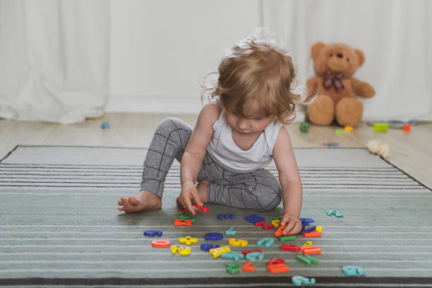 little cute toddler playing with toy letters sitting on the floor stock photo