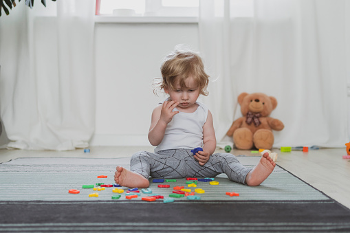 little cute toddler playing with toy letters sitting on the floor in livingroom
