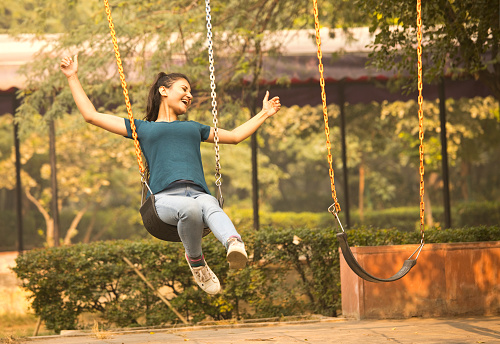Carefree woman with her arms outstretched and eyes closed enjoying swinging at park