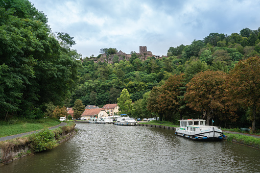 Lutzelbourg, France - September 19, 2021: Motorboat carrying tourists in a canal near commune of Lutzelbourg. Ruins of the Castle of Lutzelbourg can be seen in the distance on a hill