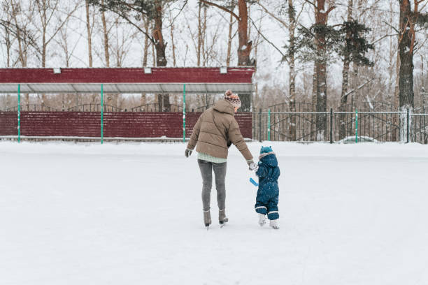 公園で母親と一緒にスケートをすることを学ぶ小さな面白い少年。アウトドア。ウィンタースポーツ - ice hockey action ice skating ice skate ストックフォトと画像