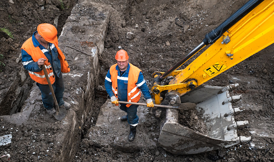 KYIV, UKRAINE - May 20, 2021: Earthworks at the construction site of the city. Repair work in the city sewerage system. Worker in a special suit with a shovel