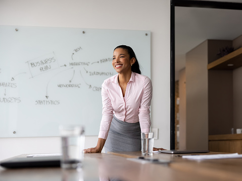 Happy African American business woman leaning on a table in the board room at the office and smiling