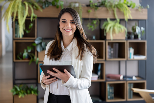 Portrait of a successful Latin American business woman using a tablet computer at the office and looking at the camera smiling