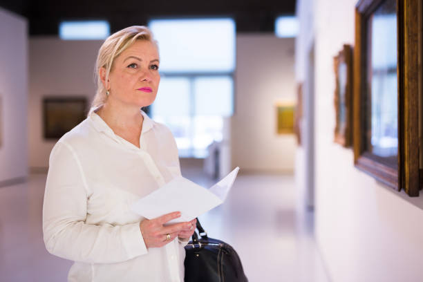 istock Senior female holding guidebook standing at exhibition 1355517051