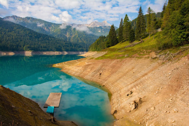Low water in Sauris Lake, Lago di Sauris, in late September. The lake is artificial, formed by a dam, and is located in Udine Province, Friuli-Venezia Giulia, north east Italy. The blue floats and platform are normally at the same level as the grass