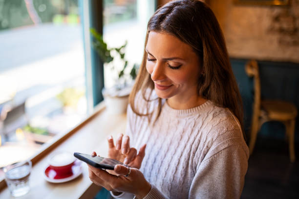 istock Young smiling woman drinking coffee and using mobile phone 1355523524