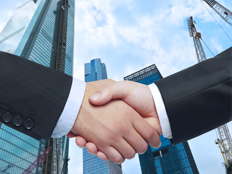 businessmen handshaking in front of construction site of a skyscraper