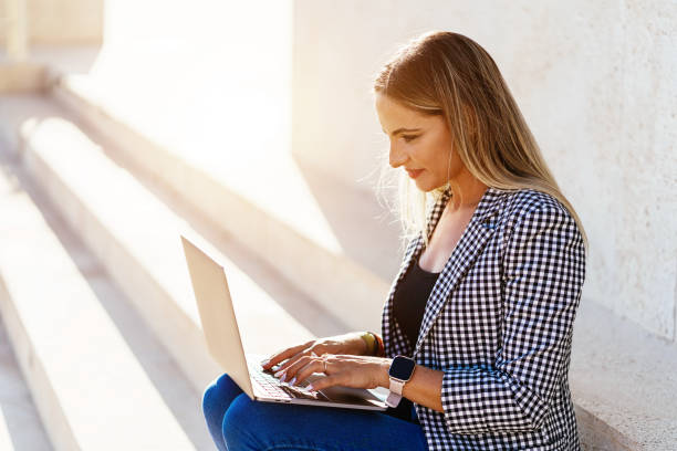 istock Smiling woman browsing laptop in street 1355524384