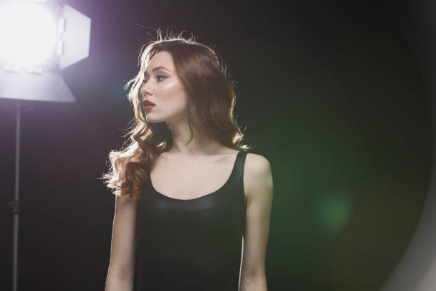 istock Charming young woman with red lips standing near studio spotlight 1355524569