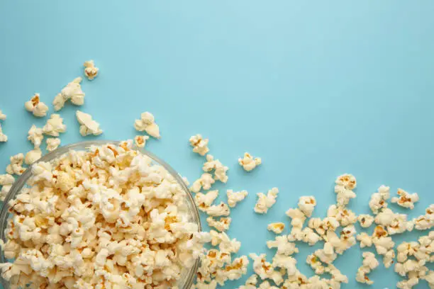 Photo of Popcorn in glass bowl on blue background.