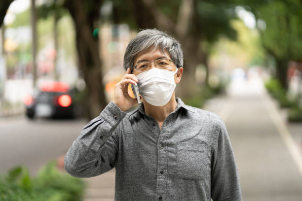 istock A senior Asian man talking into his mobile wearing a protective mask 1355527707