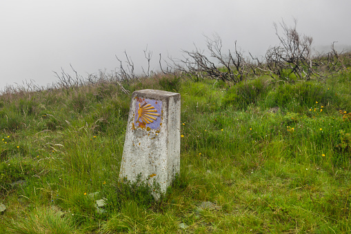 Standard concrete signpost on the Way of Saint James.\nSummer travel through the mountains along the Way of St. James (Camino de Santiago).