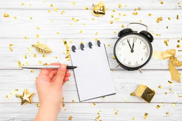 Festivedecorations and notebook with wish list and alarm  on white rustic table, flat lay style. Planning concept.