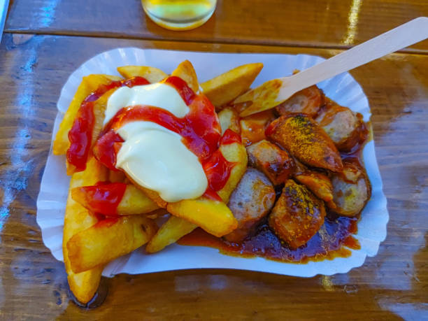 close up of female hands eating curry sausage with french fries outdoors at table