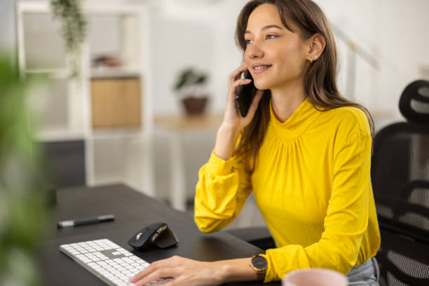 istock Young woman sitting at desk in office while talking on phone 1355534554
