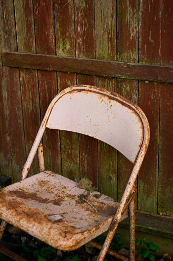 old rusted out chair against a dilapidated privacy fence