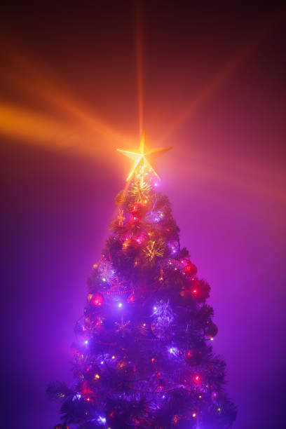 istock Christmas tree with festive lights, purple background with mist 1355537716